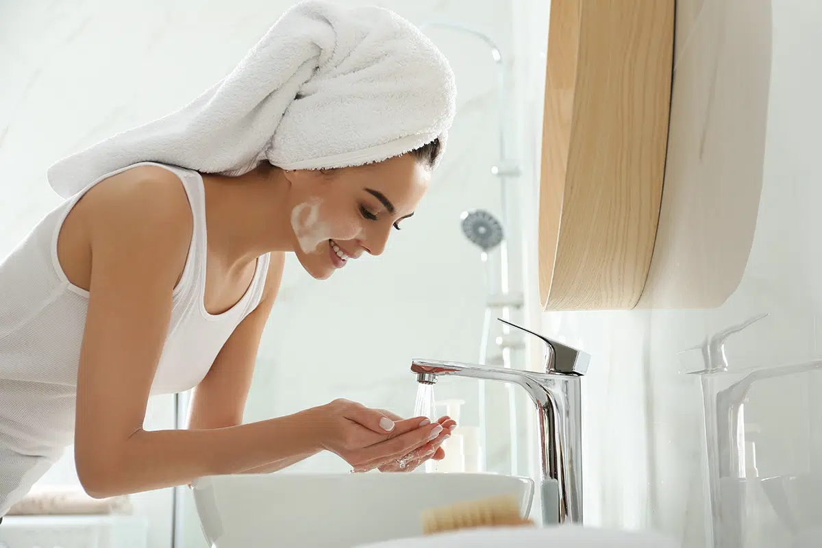 Happy young woman washing face in bathroom