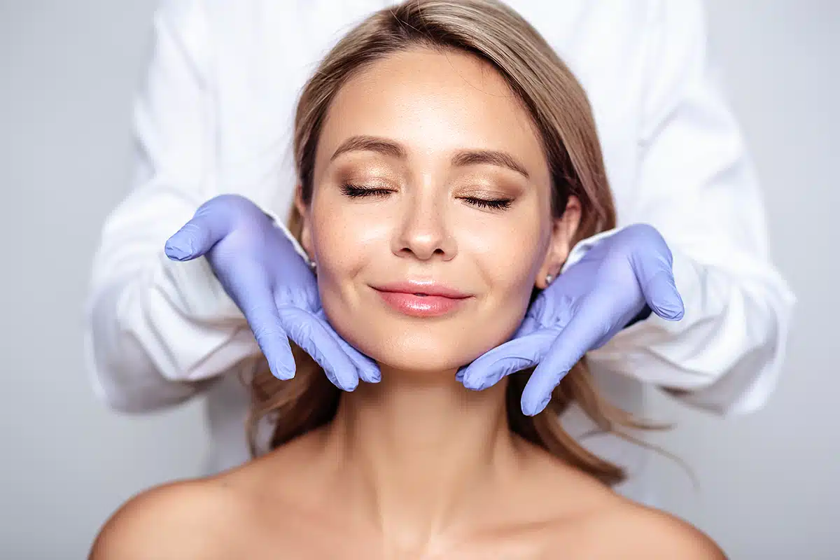 Young blonde woman with cosmetologyst hands in gloves